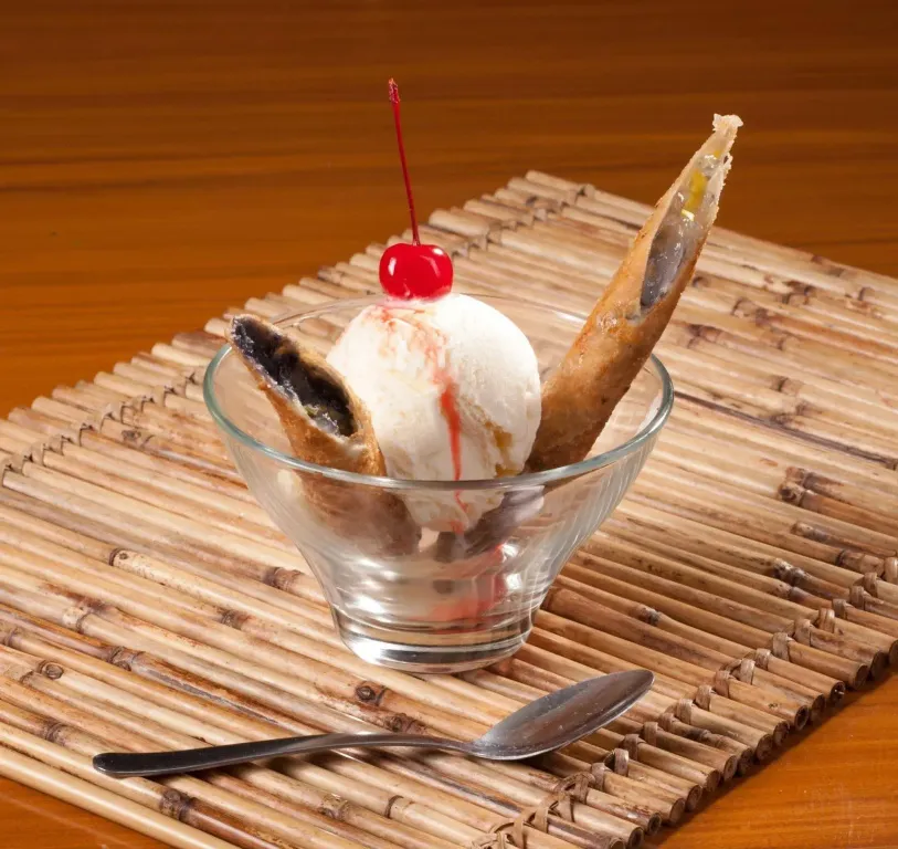 Une glace à la vanille servie dans un verre avec des gaufrettes et une cerise au sommet.