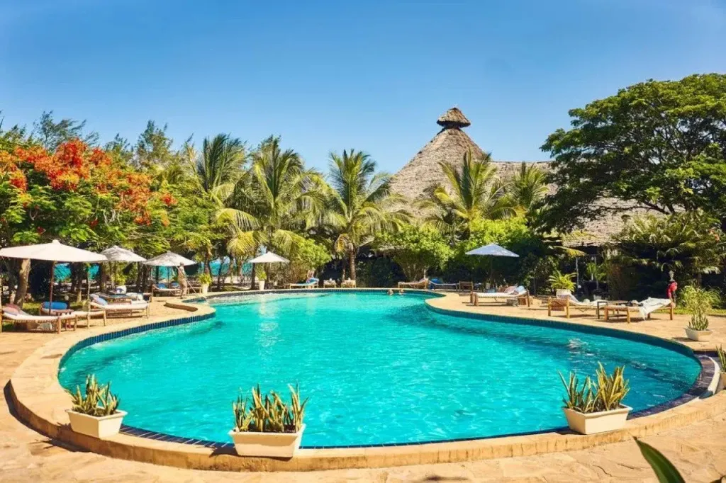 Une piscine turquoise bordée de transats et de parasols, dans un cadre tropical luxuriant.