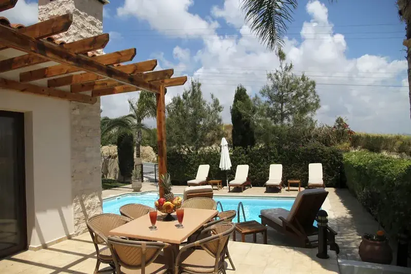 Une table à manger est placée sur une terrasse ombragée près d'une piscine.