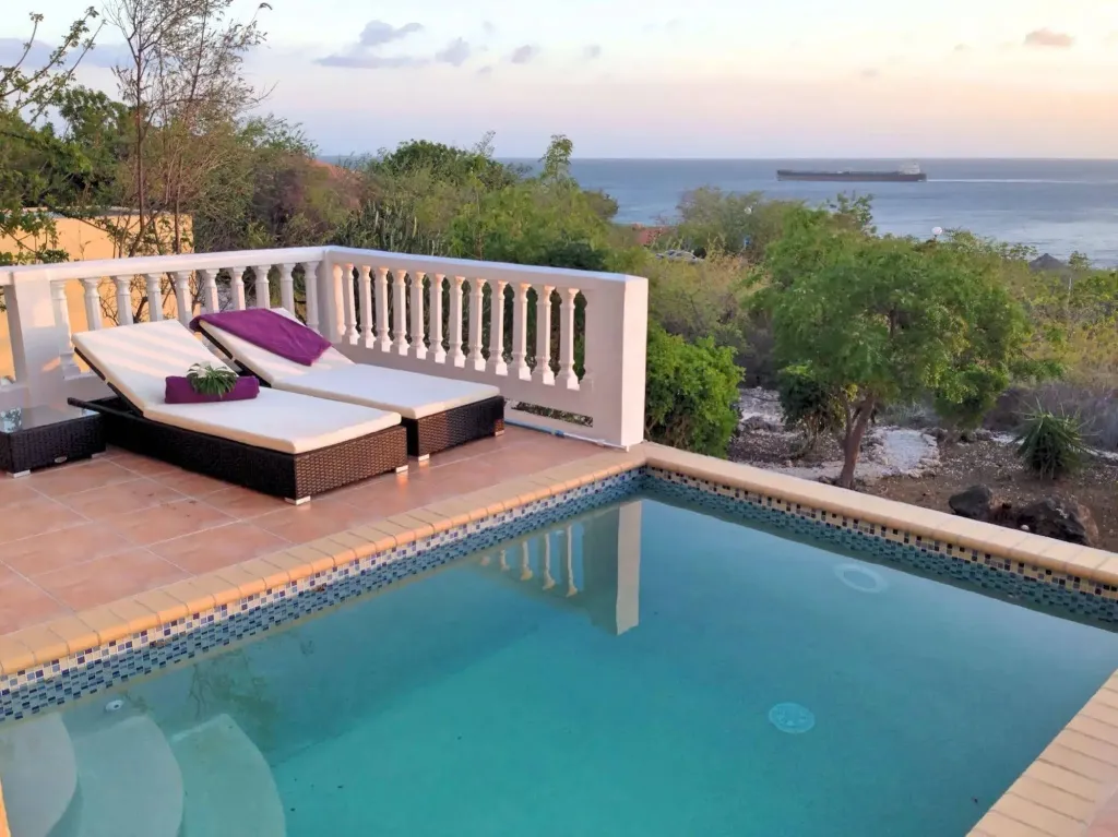 Deux transats invitent à la détente au bord d'une piscine turquoise avec vue sur la mer.