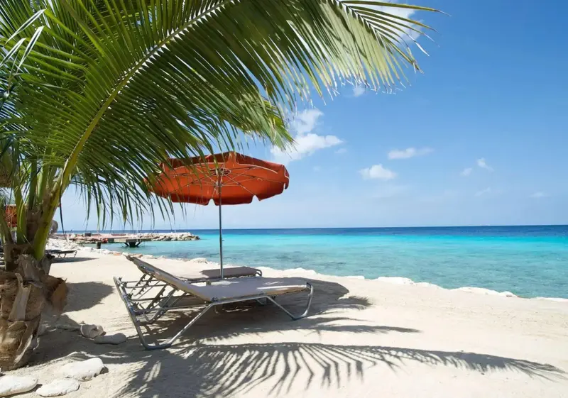 Transats et parasol sur une plage de sable blanc bordée d'eau turquoise.
