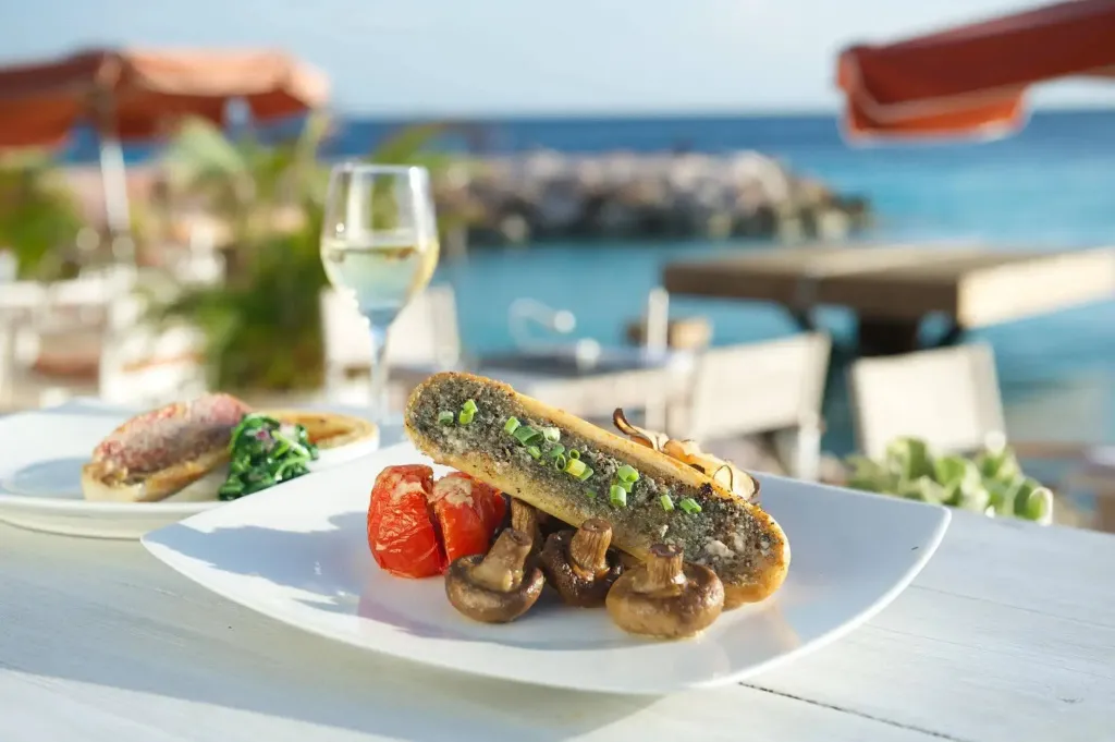 Assiette de poisson grillé accompagnée de légumes et de champignons, sur une table en extérieur face à la mer.