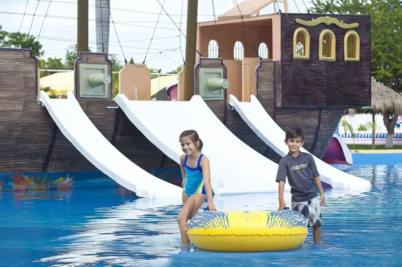 Deux enfants se tiennent dans une piscine avec des toboggans aquatiques en arrière-plan.