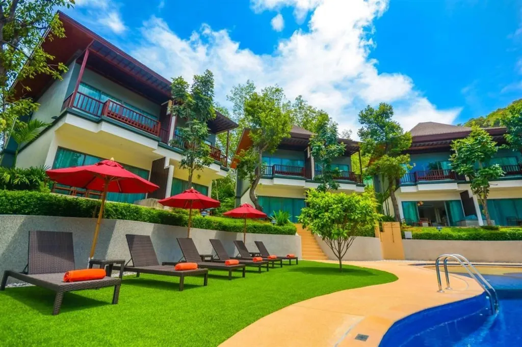 Transats rouges et parasols sur une pelouse verte près d'une piscine.