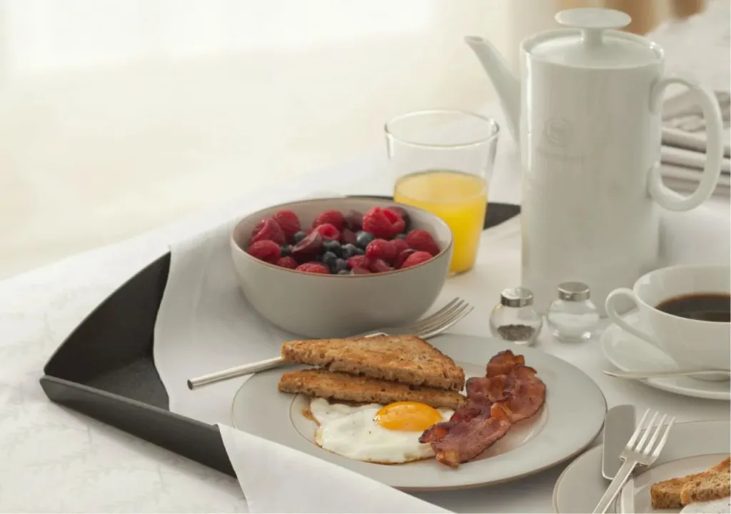 Un plateau de petit-déjeuner avec des fruits rouges, des œufs, du bacon et des boissons.
