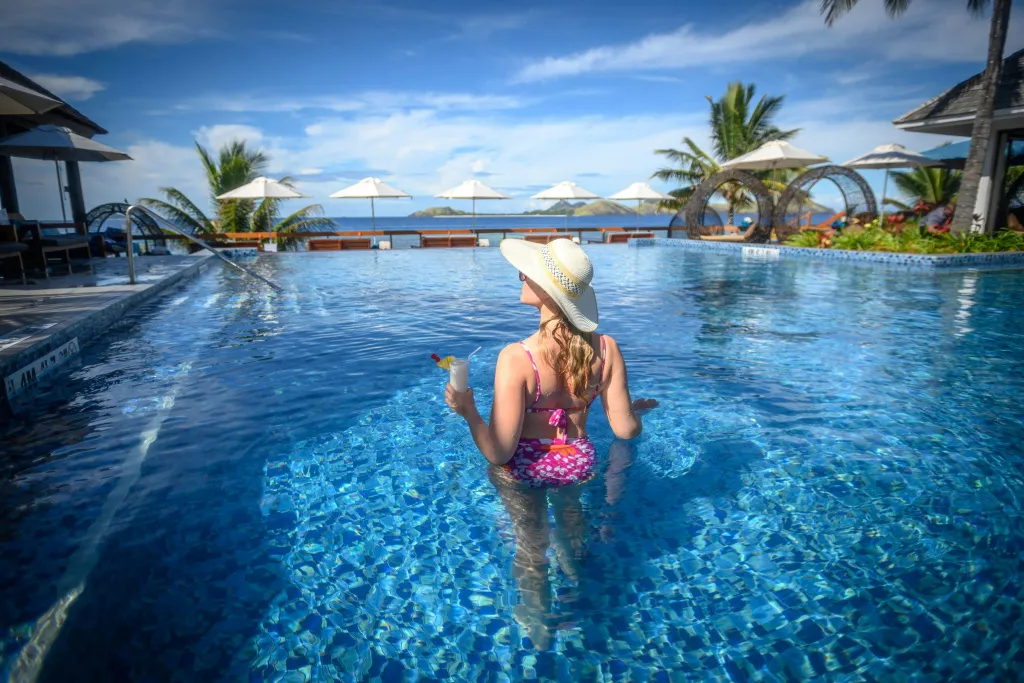 Une personne dans une piscine avec un cocktail à la main.