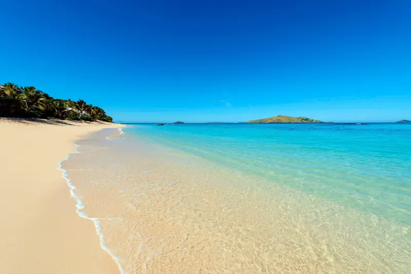 Une plage de sable fin bordée d'une eau turquoise et d'une végétation luxuriante.