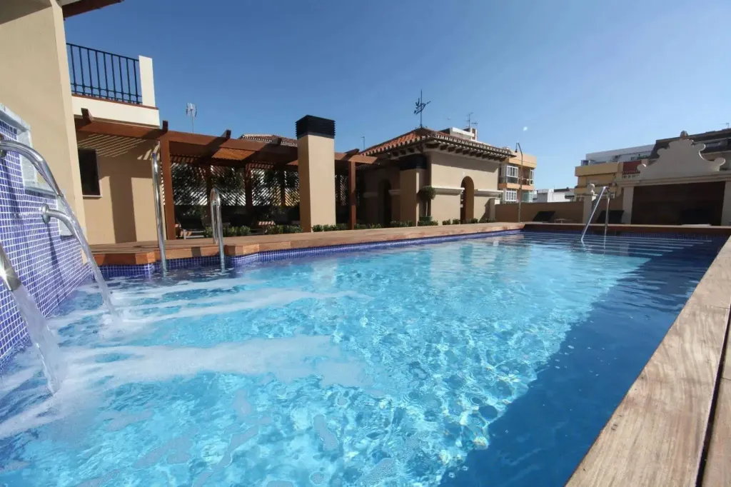 Une piscine rectangulaire avec une cascade et une zone de repos ombragée.