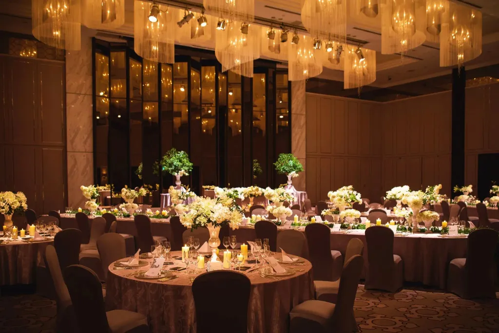 Une salle de réception élégante est mise en scène avec des tables rondes nappées et décorées de compositions florales.