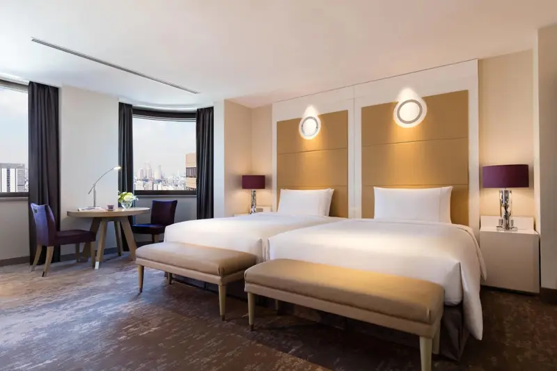 Une chambre lumineuse avec deux lits simples et un coin repas près de la fenêtre.