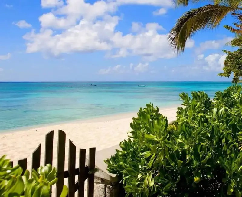 Une plage de sable blanc bordée d'une mer turquoise sous un ciel nuageux.