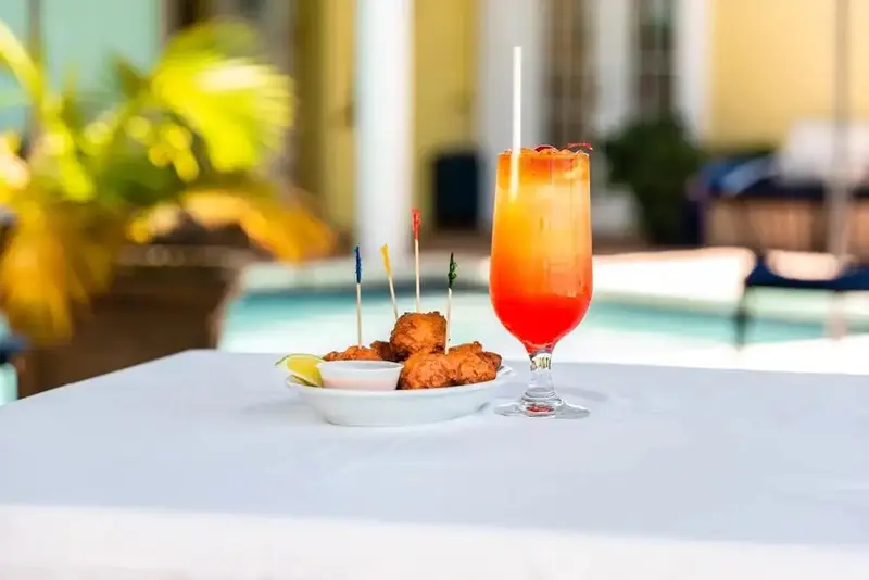 Un cocktail coloré et des amuse-gueules sont servis sur une table blanche près d'une piscine.