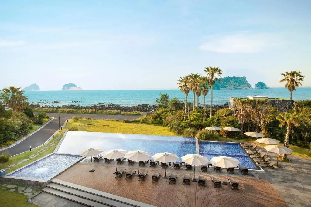 Piscine à débordement avec transats et parasols, vue sur la mer et les îles.