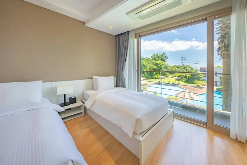 Chambre lumineuse avec deux lits simples et vue sur une piscine.