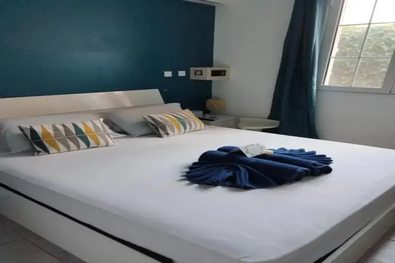 Une chambre lumineuse avec un grand lit blanc et un mur bleu turquoise.