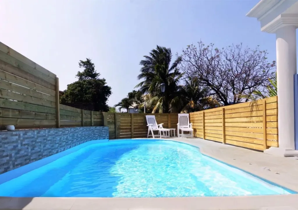 Petite piscine rectangulaire entourée d'une terrasse en bois et d'une clôture.