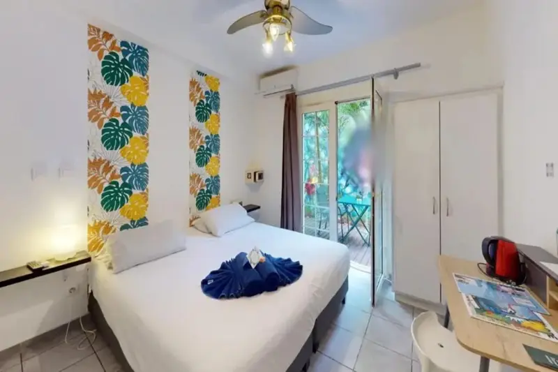 Une chambre lumineuse avec un lit recouvert d'une décoration en forme de poisson et une terrasse accessible par des baies vitrées.