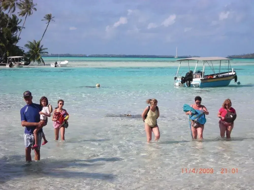 Des personnes marchent dans une eau turquoise peu profonde sur une plage ensoleillée.
