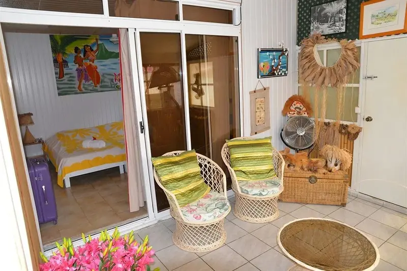 Espace de détente avec des fauteuils en rotin et une chambre visible à travers des baies vitrées.