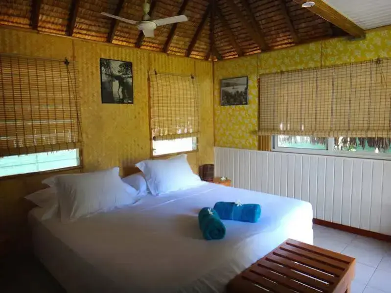 Une chambre lumineuse avec un lit recouvert de draps blancs et des stores en bambou.