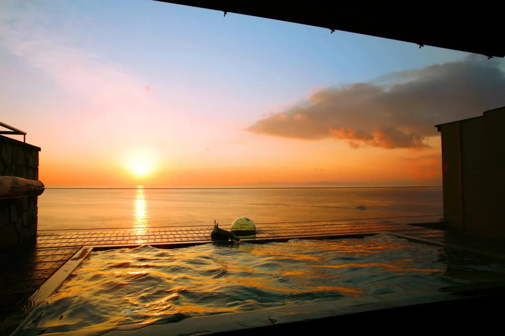 Une piscine à débordement offre une vue sur un coucher de soleil orangé sur la mer.