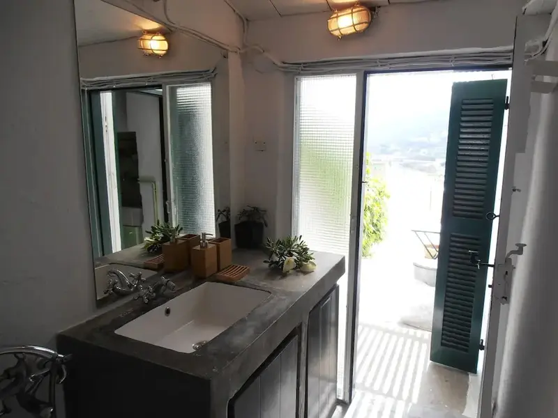 Une salle de bain lumineuse avec un grand miroir et une porte ouverte sur une vue verdoyante.