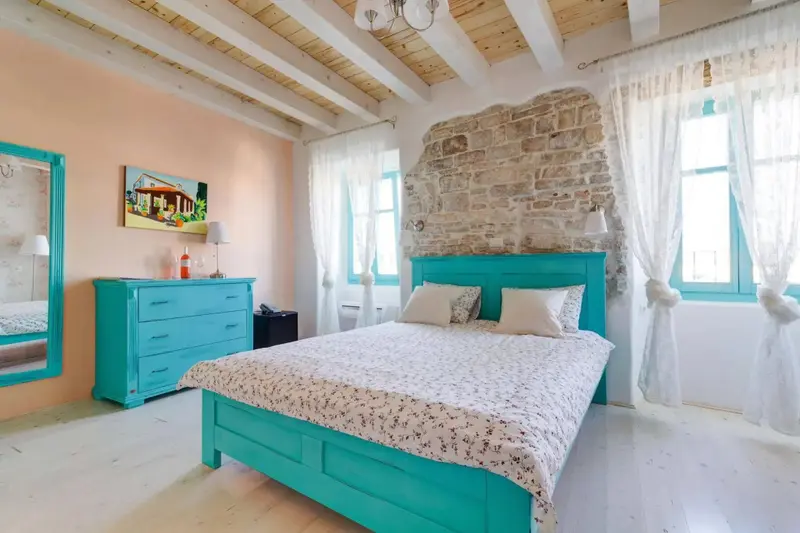 Une chambre lumineuse avec un lit recouvert d'une couette fleurie et un mur en pierre.