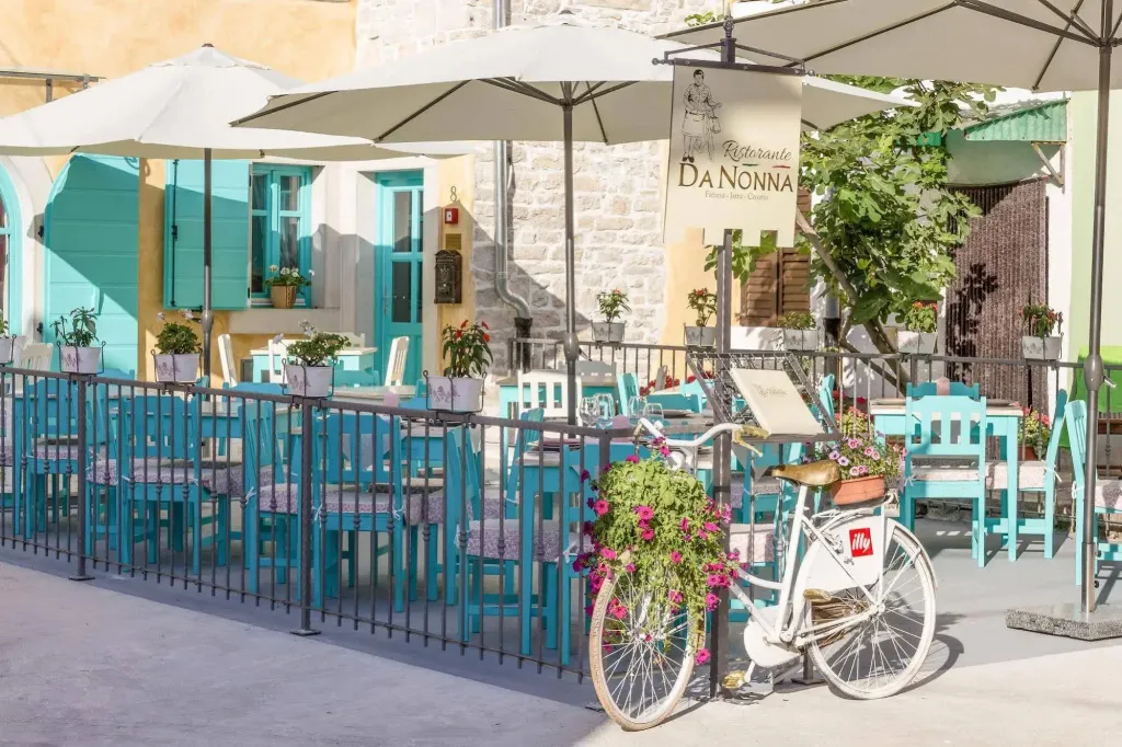 Terrasse ombragée avec tables et chaises bleues devant un bâtiment en pierre.