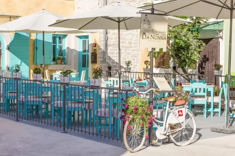 Terrasse ombragée avec tables et chaises bleues devant un bâtiment en pierre.