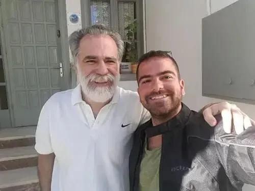Deux hommes souriants posent devant une porte et une fenêtre.
