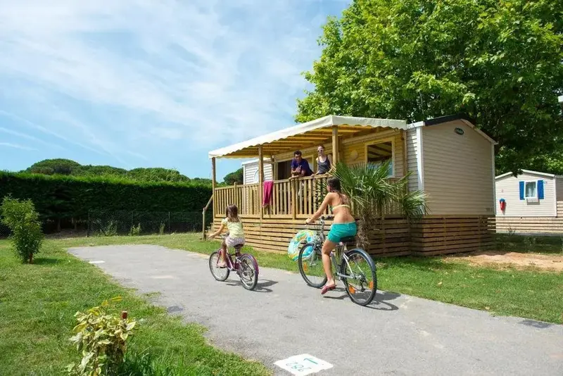 Une famille se promène à vélo devant un bungalow avec terrasse.