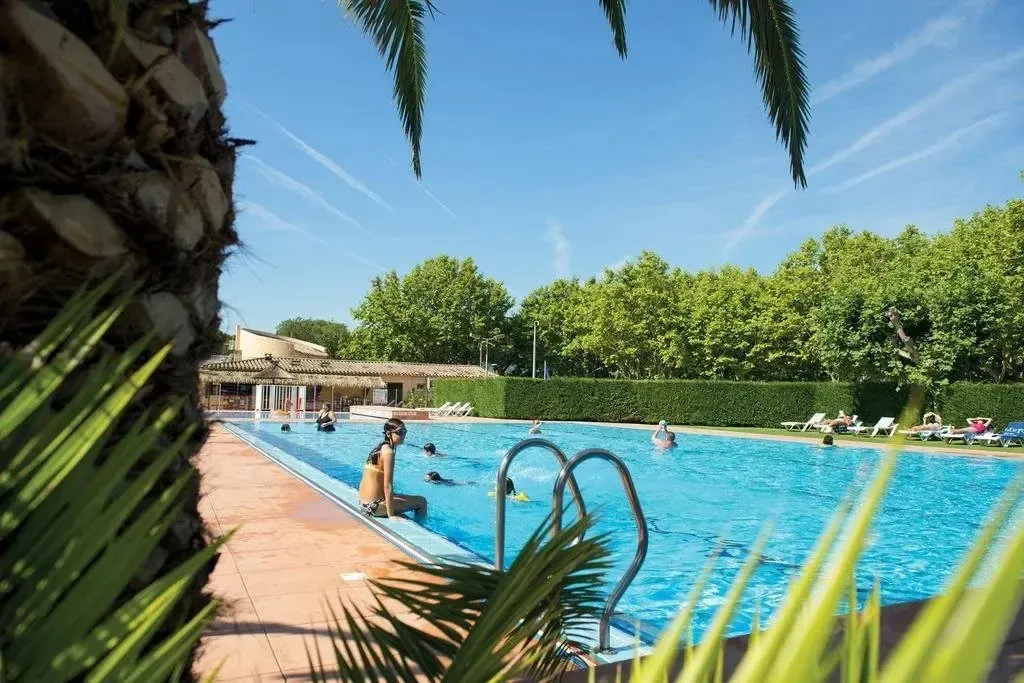 Une piscine ensoleillée avec des personnes se baignant et se relaxant au bord.