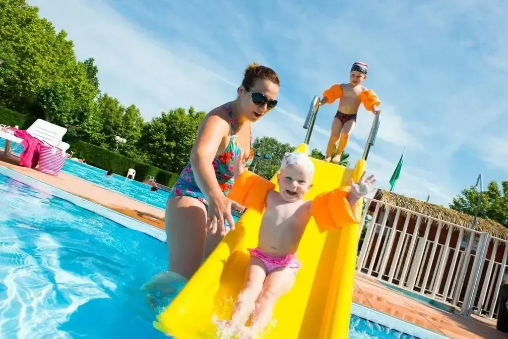 Une femme et deux enfants s'amusent au bord d'une piscine ensoleillée.