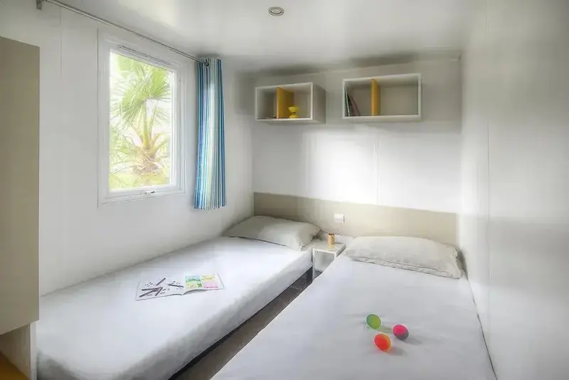 Une chambre lumineuse avec deux lits simples et une fenêtre donnant sur la végétation.