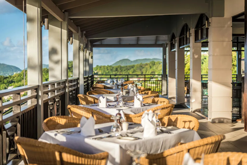Une salle à manger extérieure avec des tables dressées offre une vue sur un paysage verdoyant.