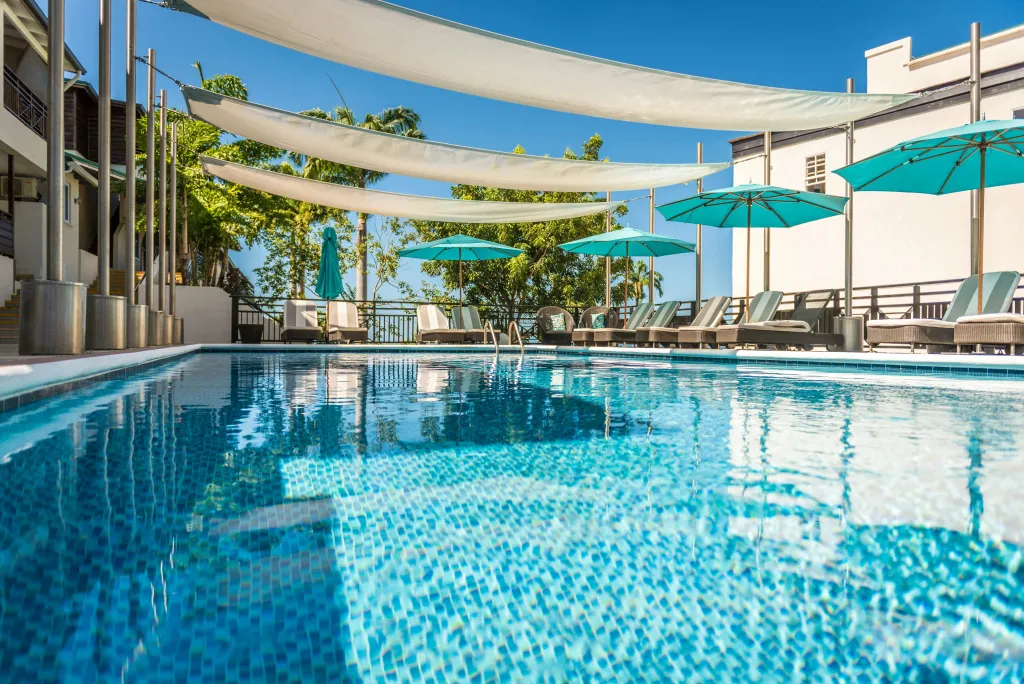 Une piscine rectangulaire turquoise est entourée de transats sous des parasols.