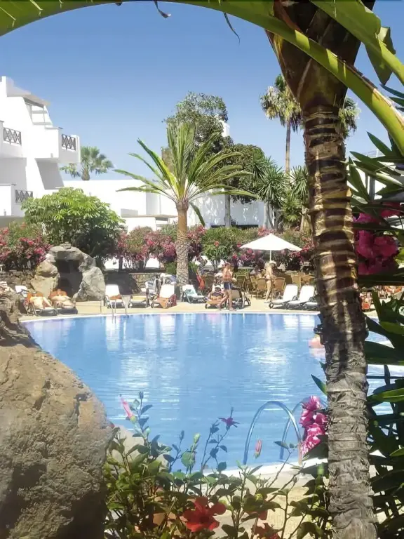 Une piscine bordée de transats et de végétation luxuriante sous un ciel bleu.