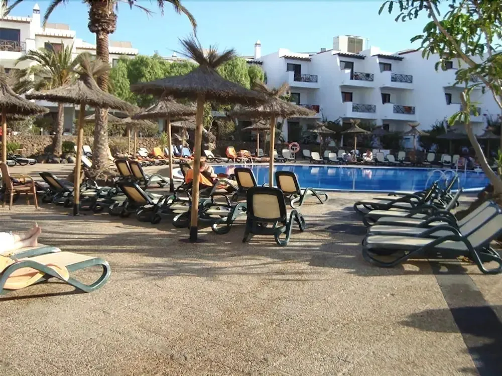 Transats et parasols ombragent une piscine rectangulaire bordée d'une terrasse.