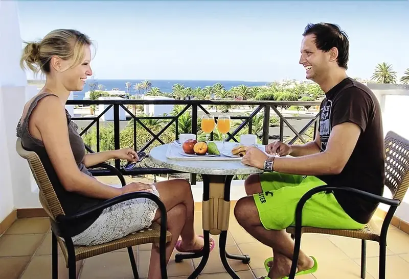 Un couple prend son petit-déjeuner sur un balcon ensoleillé avec vue sur la mer.