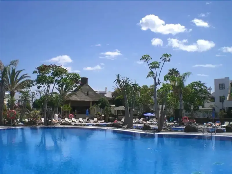 Piscine bleue entourée de transats et de végétation luxuriante sous un ciel clair.