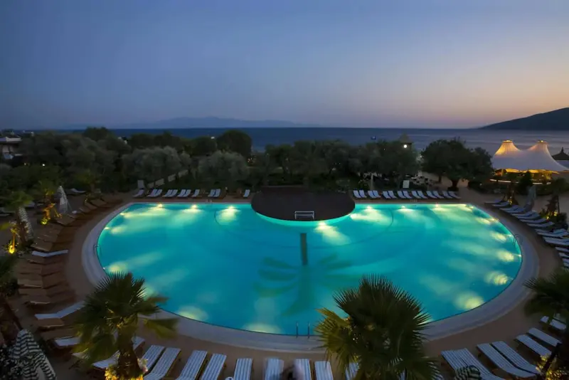 Une piscine illuminée au crépuscule, entourée de transats et de végétation.