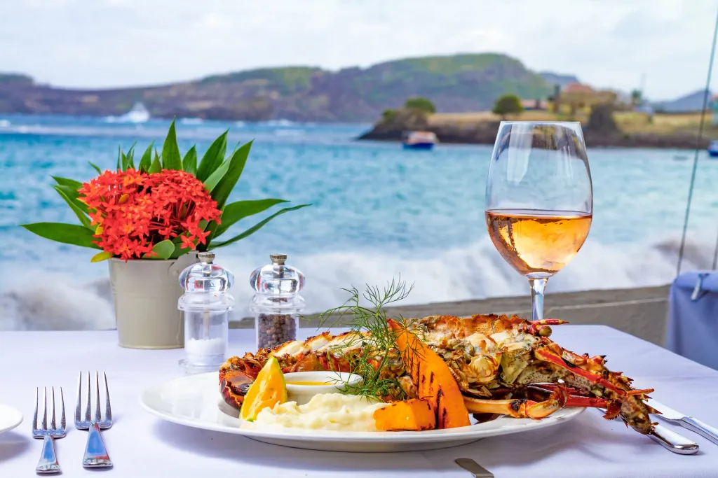 Une table dressée avec un plat de fruits de mer et une boisson face à la mer.