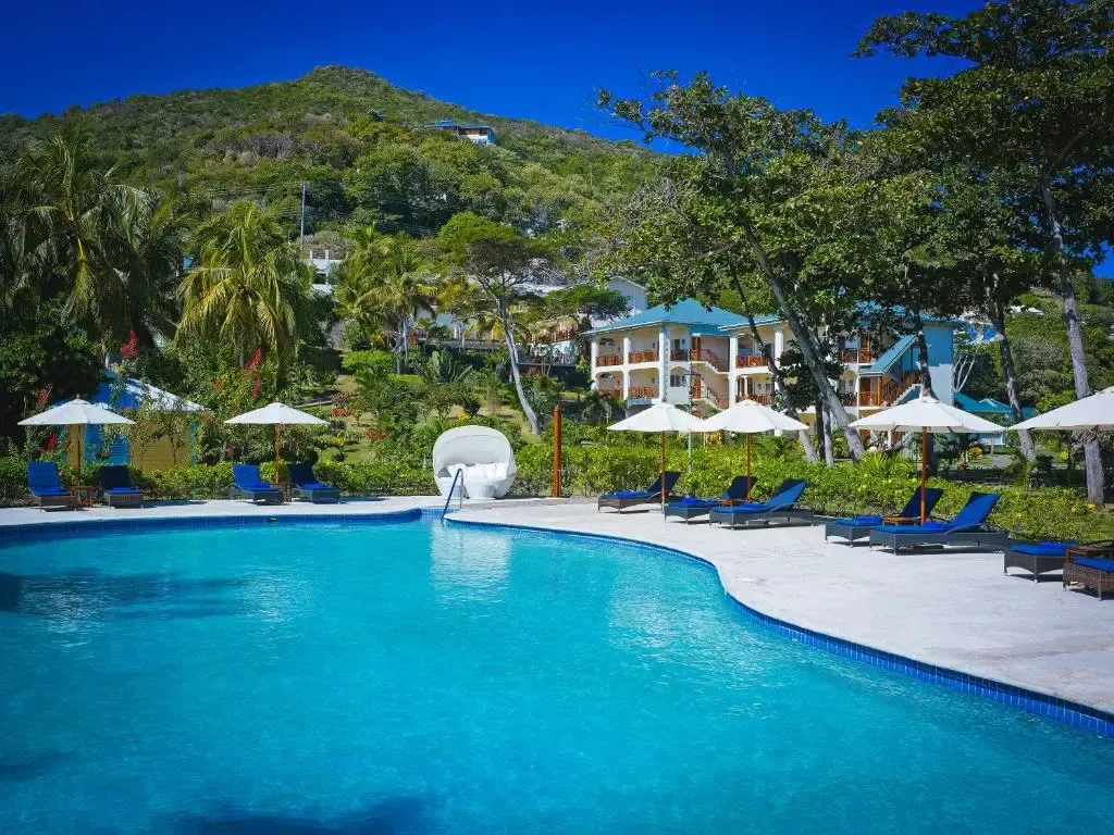 Une piscine bleue bordée de transats et de parasols, avec des bâtiments en arrière-plan.