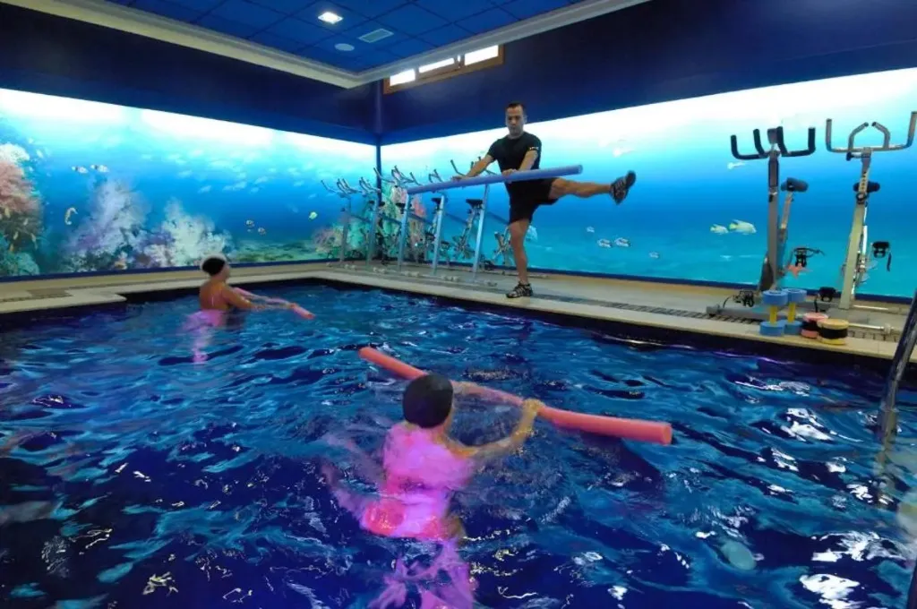 Des personnes pratiquent une activité physique dans une piscine décorée d'un paysage marin.