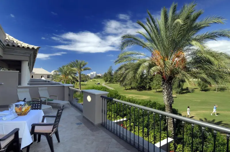 Une table dressée sur une terrasse offre une vue sur un terrain de golf verdoyant sous un ciel bleu.