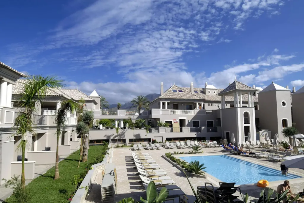Vue d'un complexe hôtelier avec piscine et transats sous un ciel bleu.