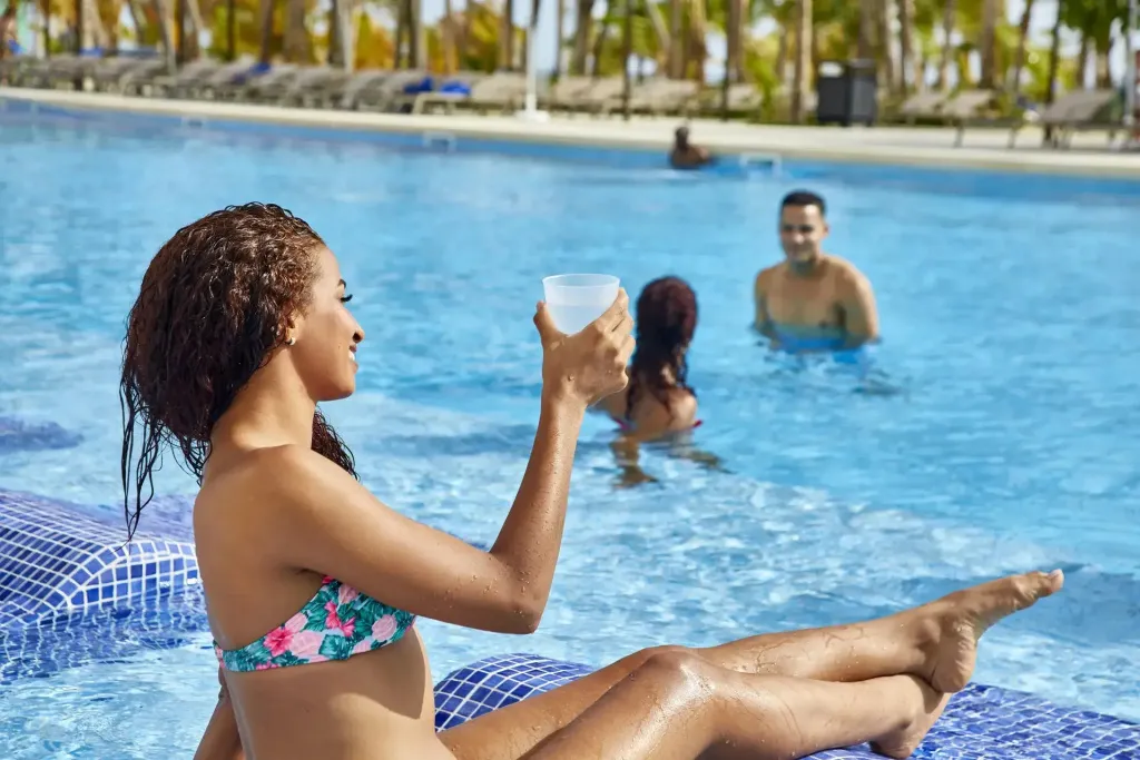 Une femme se détend au bord d'une piscine ensoleillée avec un verre à la main.