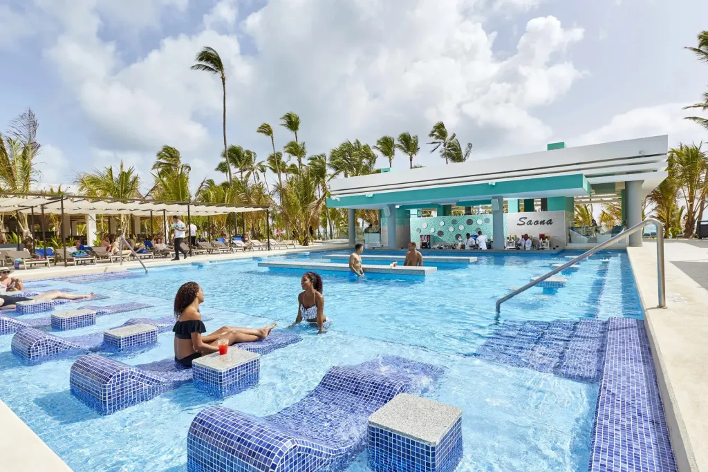 Des clients se détendent au bord d'une piscine turquoise avec un bar intégré.