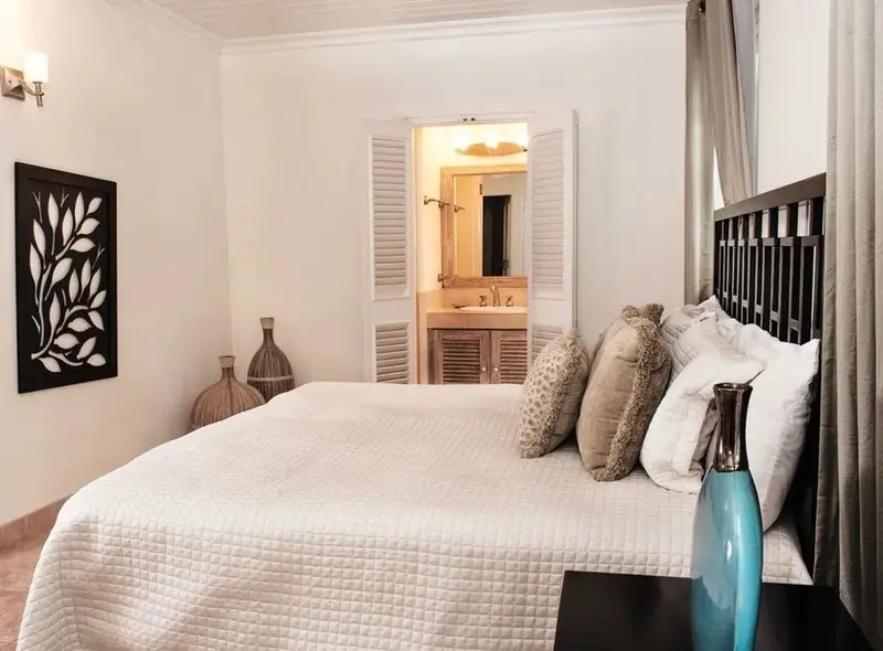 Une chambre lumineuse avec un grand lit recouvert d'une courtepointe blanche et de coussins.