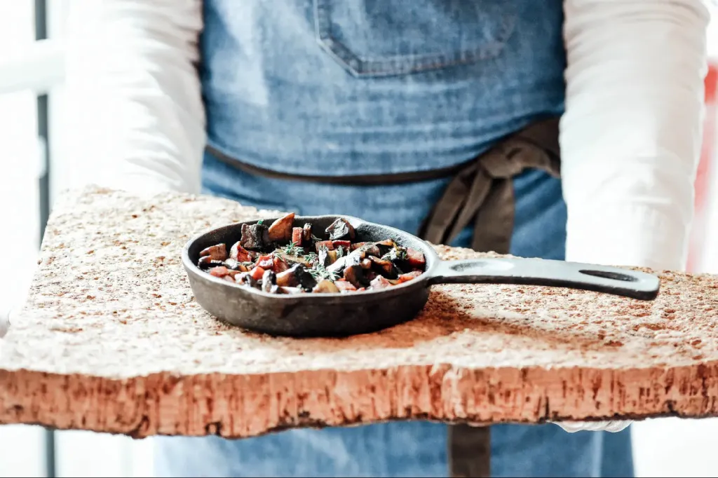 Une poêle en fonte contenant un plat est présentée sur une planche en bois.